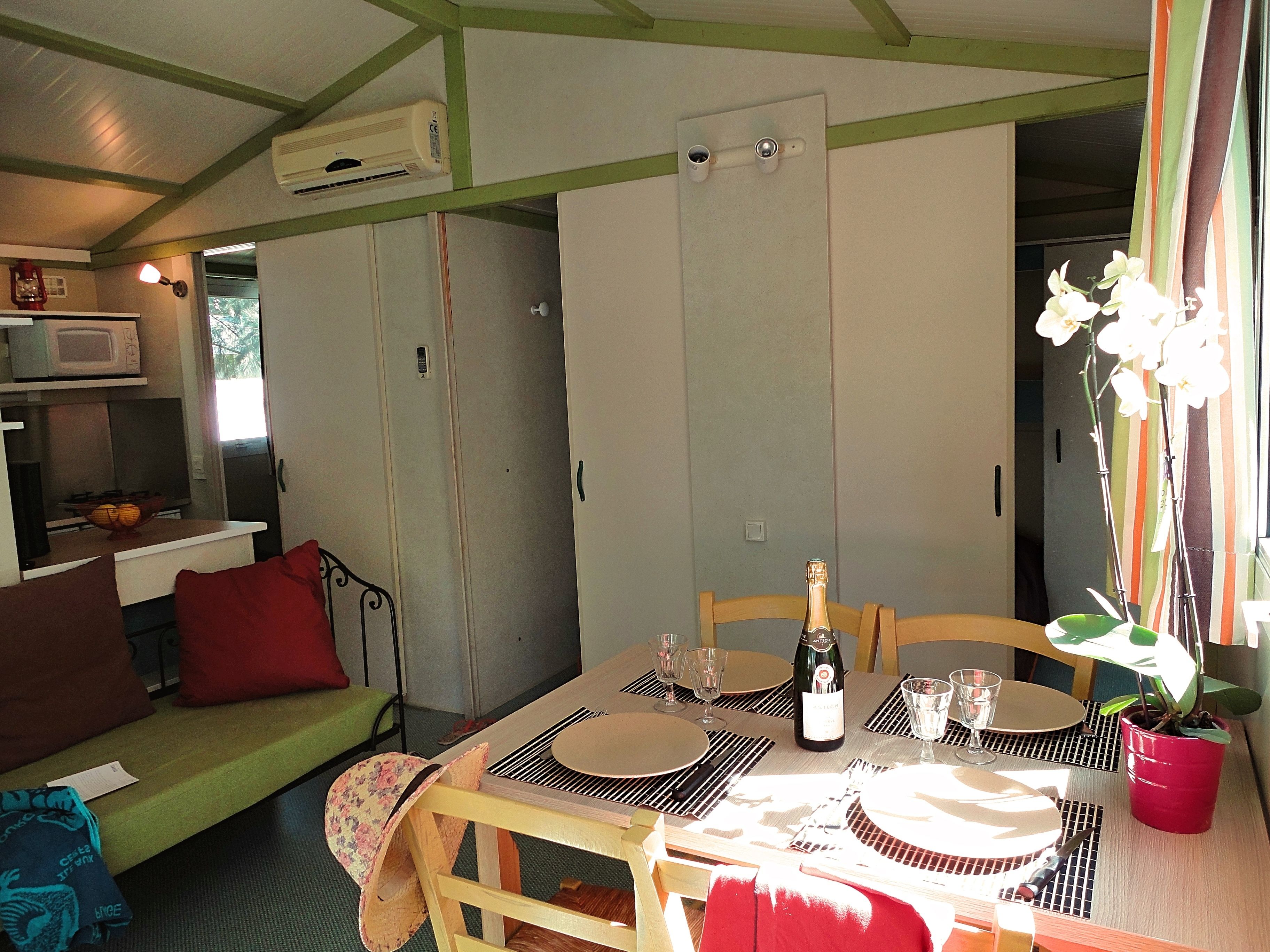 Un coin repas avec une table dressée pour quatre personnes, une bouteille de champagne et une orchidée en pot.