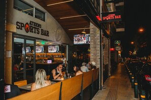 A sports bar with outdoor seating, a bar area with a counter, and a TV screen displaying sports.