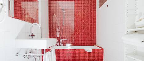 Un baño moderno con pared de ducha en mosaicos rojos, un lavabo blanco y una bañera.