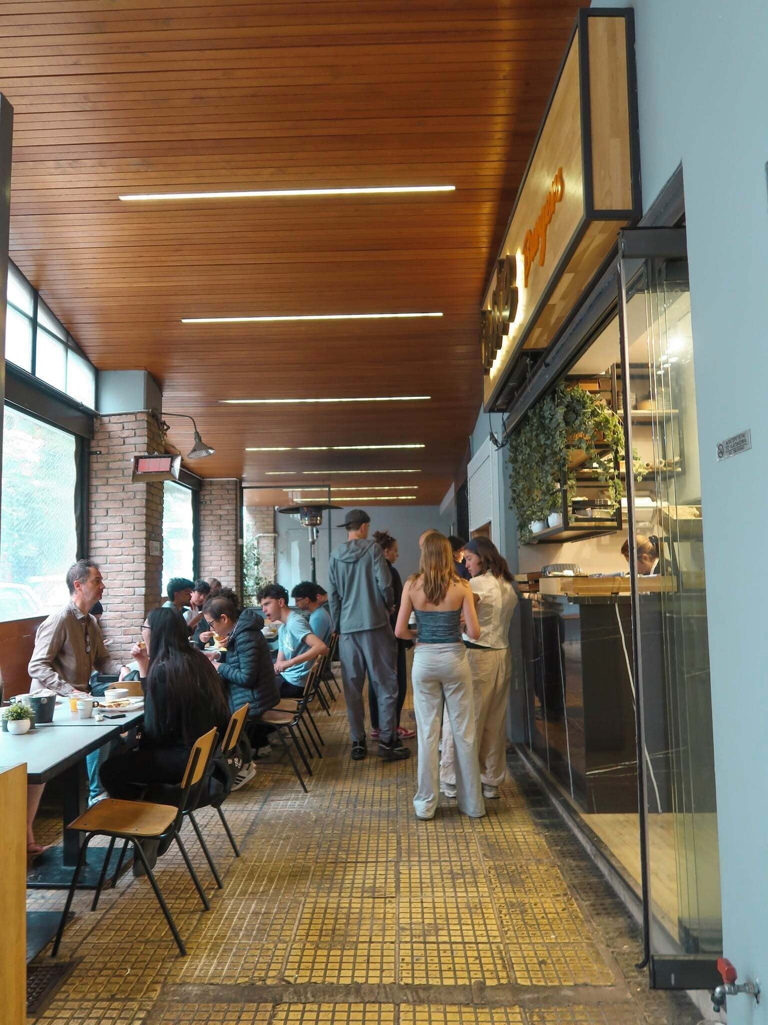 A restaurant with wooden ceiling, tiled floor, and a counter with a plant.