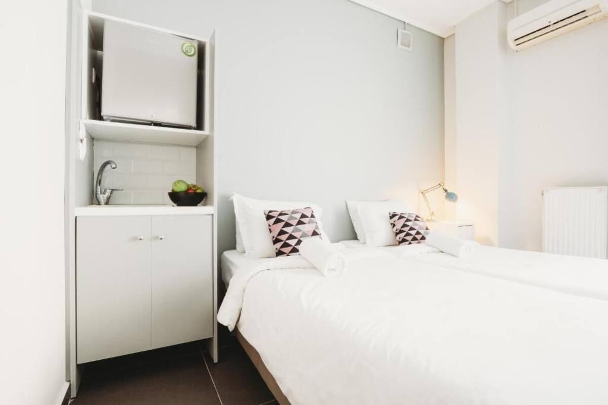 A hotel room with a bed, a small kitchenette, a sink, and an air conditioning unit.