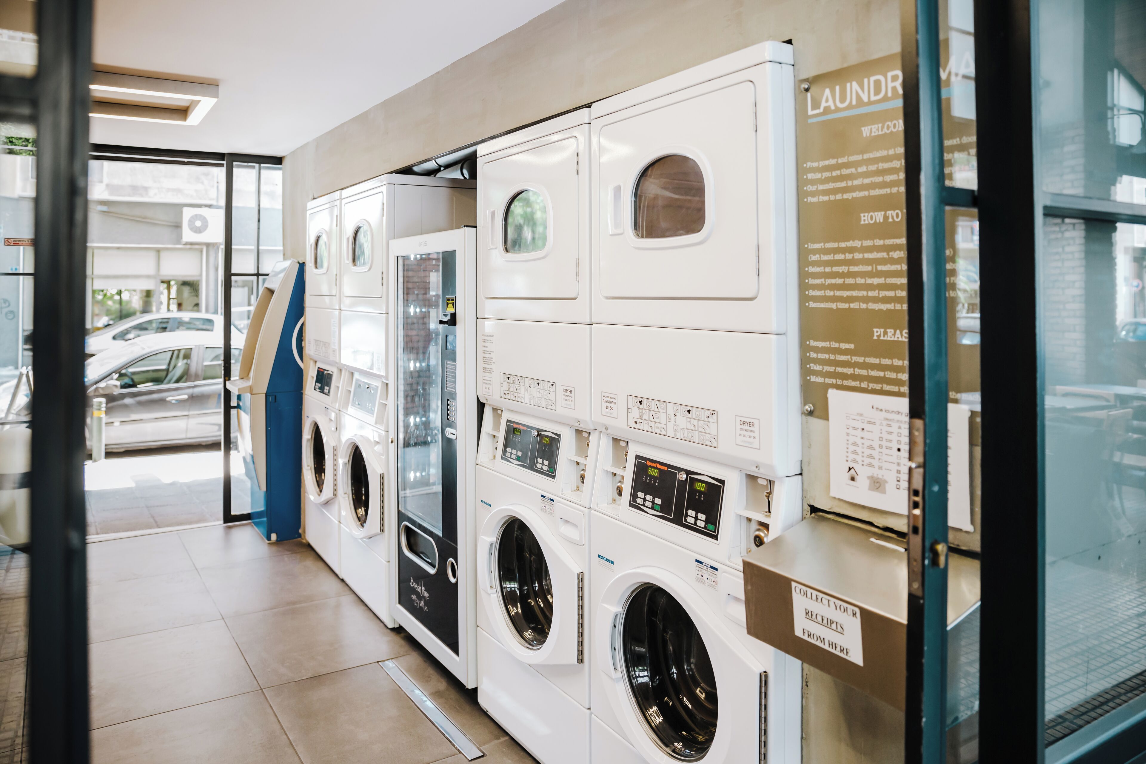 A laundromat with multiple washing machines and dryers, a glass door entrance, and a sign with instructions.