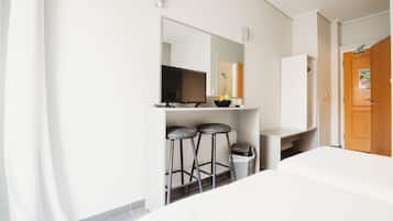 A hotel room with a bed, a TV, a mirror, two stools, and a wooden door.