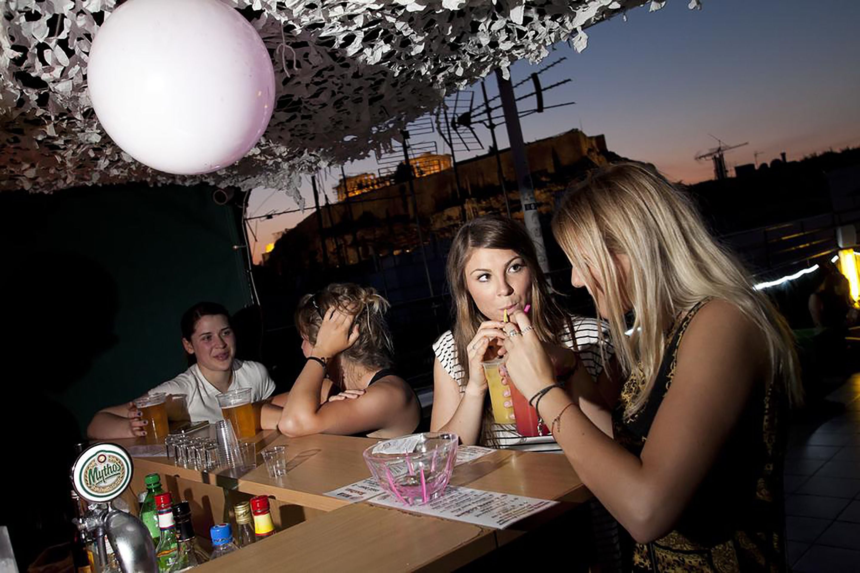 A group of people sitting at a table with drinks and bottles, in an outdoor setting with a decorative ceiling.
