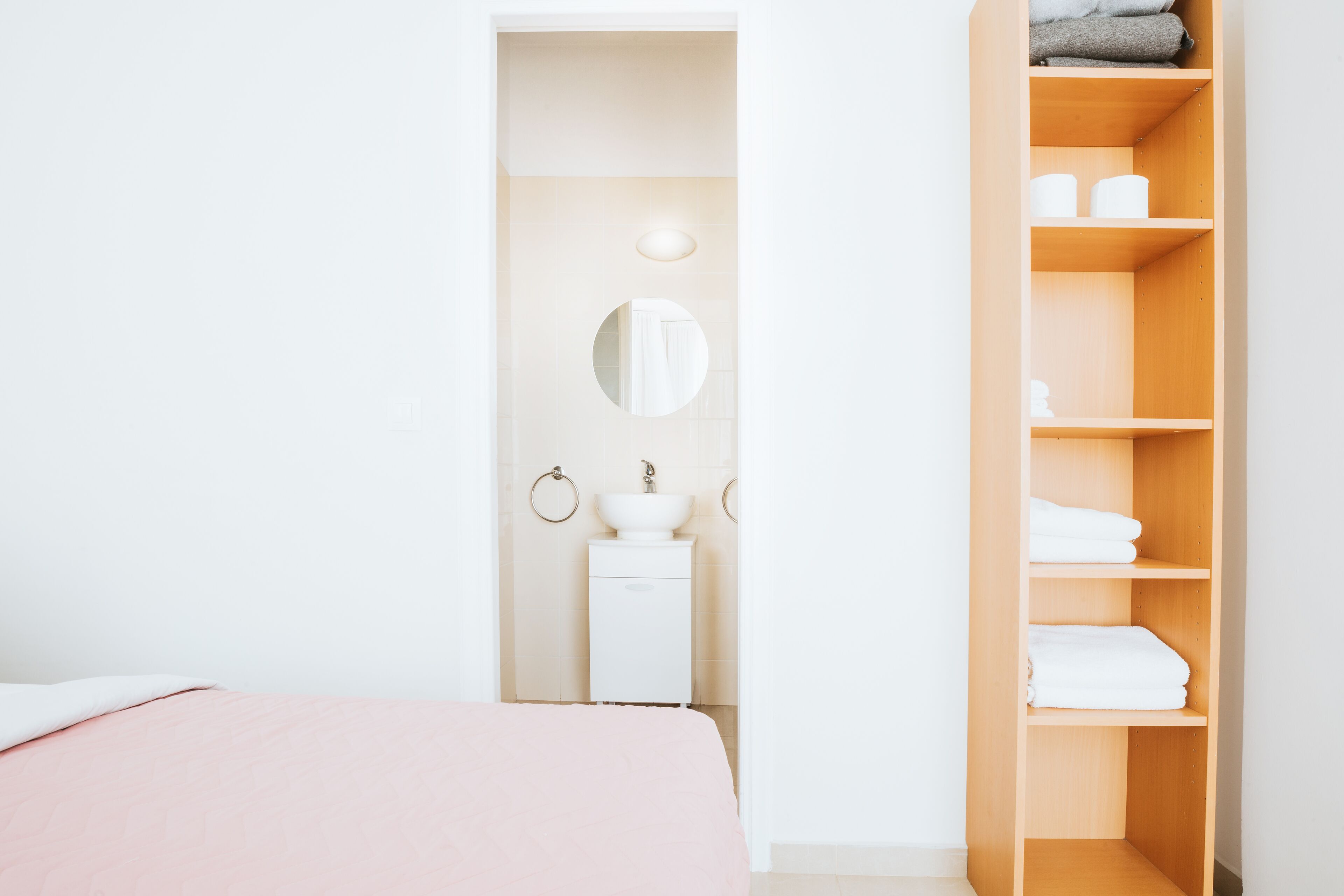 Une chambre à coucher avec un lit, une table de chevet blanche, un miroir et une armoire en bois avec des étagères.