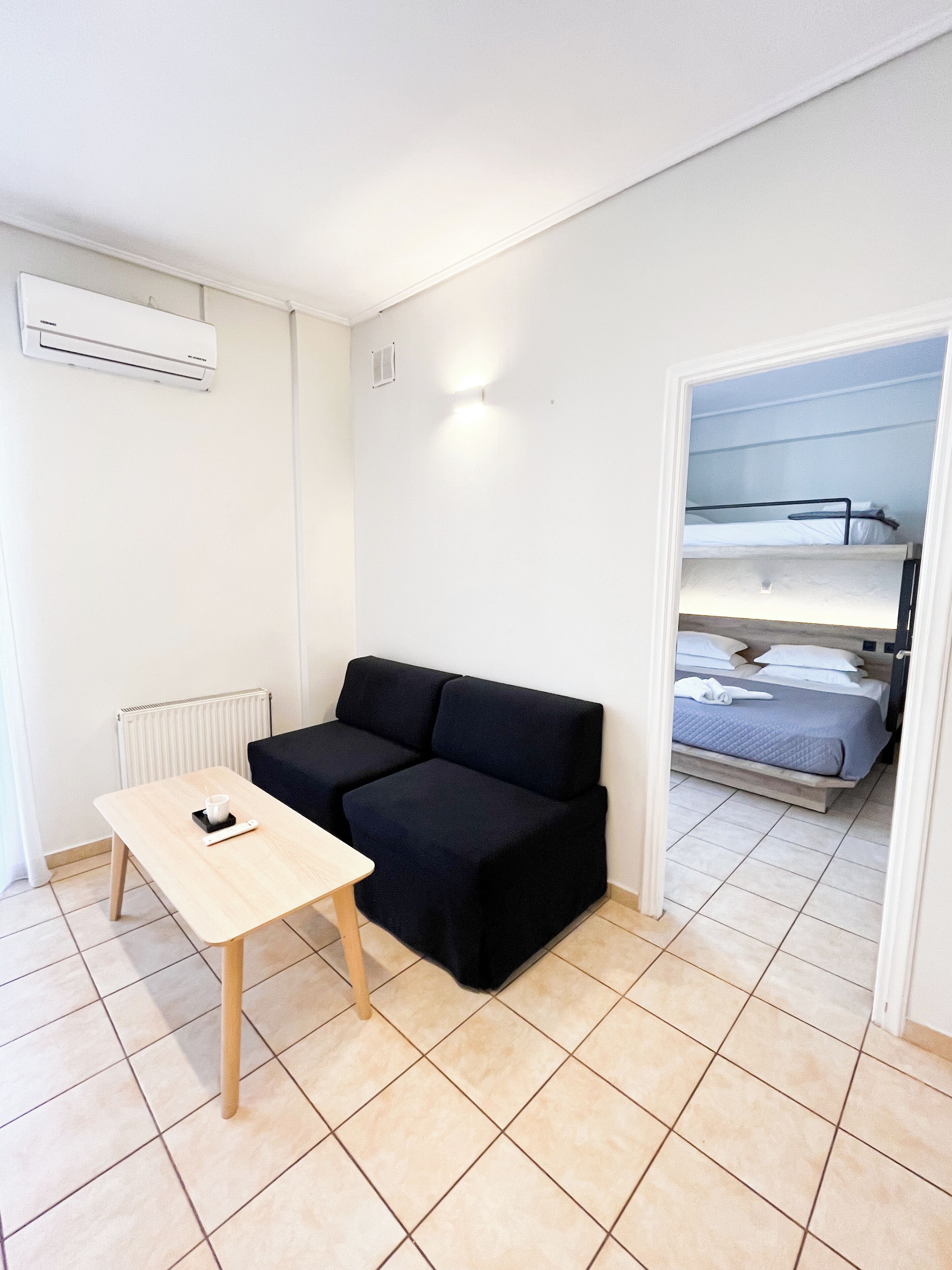 A small, tidy room with a black sofa, a wooden table, and a bunk bed in the background.