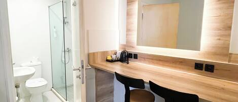 A modern bathroom with a glass shower enclosure, a toilet, and a sink. There is a wooden vanity with a mirror above it and two stools.