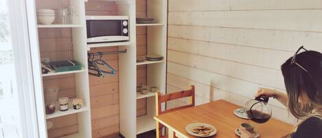 Una cocina compacta con microondas, estantes y una mesa de comedor con un plato de galletas.