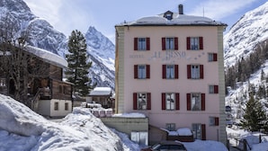 A pink building labeled "HOTEL LE BESSO" with multiple windows and a snow-covered roof, surrounded by snow and mountains. - Hotel Besso (Anniviers)