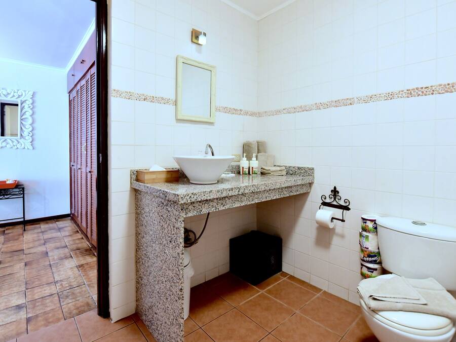 Un baño con lavamanos, espejo, inodoro y paredes de azulejos.