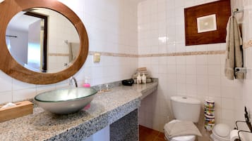 Un baño con encimera de granito, un espejo redondo, un inodoro y un perchero.