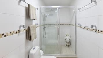 Een badkamer met een douchecabine van glas, witte tegels en een klein decoratief tafeltje.