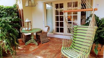 Un patio con una silla de mimbre, una mesa y una hamaca colgante.