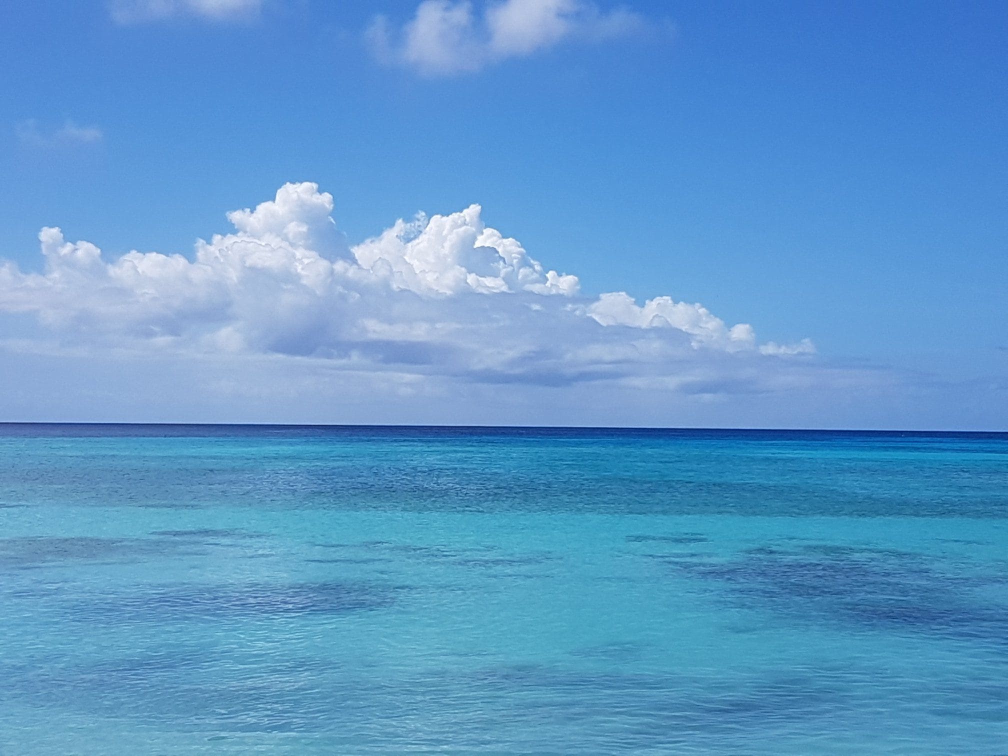 Una vista despejada de un océano turquesa bajo un cielo azul brillante con nubes dispersas.