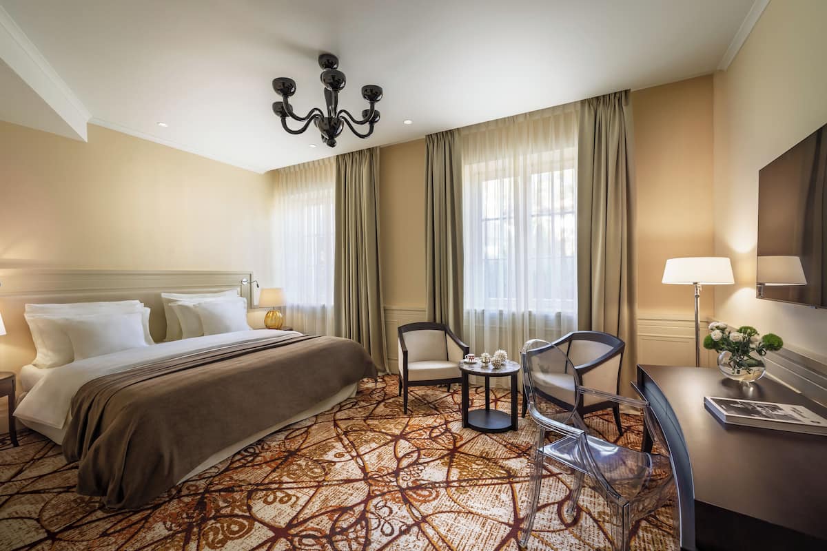 Ein Hotelzimmer mit einem großen Bett, zwei Stühlen, einem Schreibtisch und einer Chandelier.