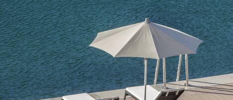 Zona junto a la piscina con dos sillones de descanso y una mesa, con vistas a una extensión de agua.