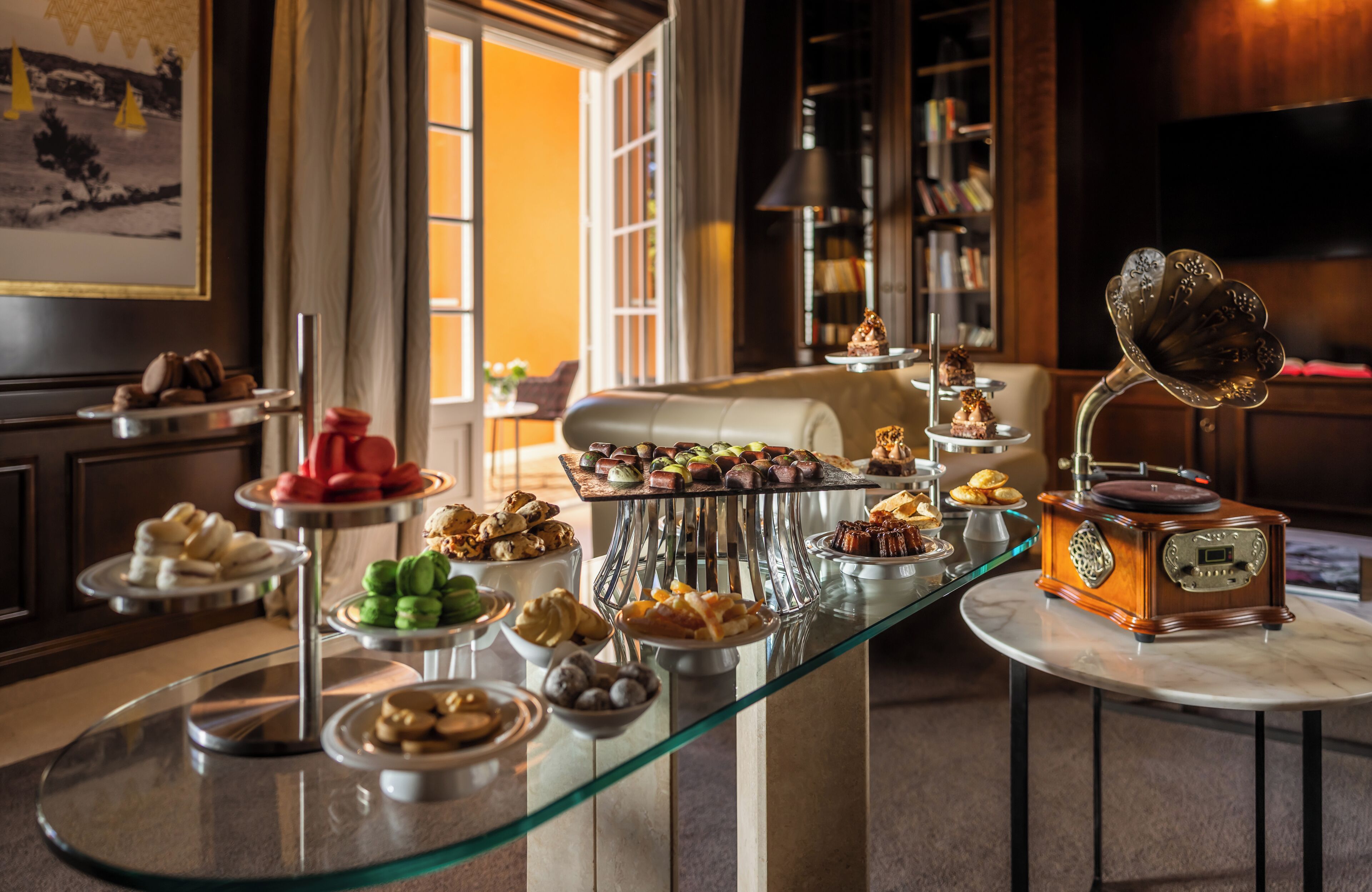 Een buffet met diverse gebakjes en desserts, een grammofoon en een boekenkast op de achtergrond.