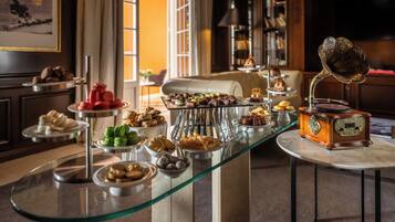 Een buffet met diverse gebakjes en desserts, een grammofoon en een boekenkast op de achtergrond.