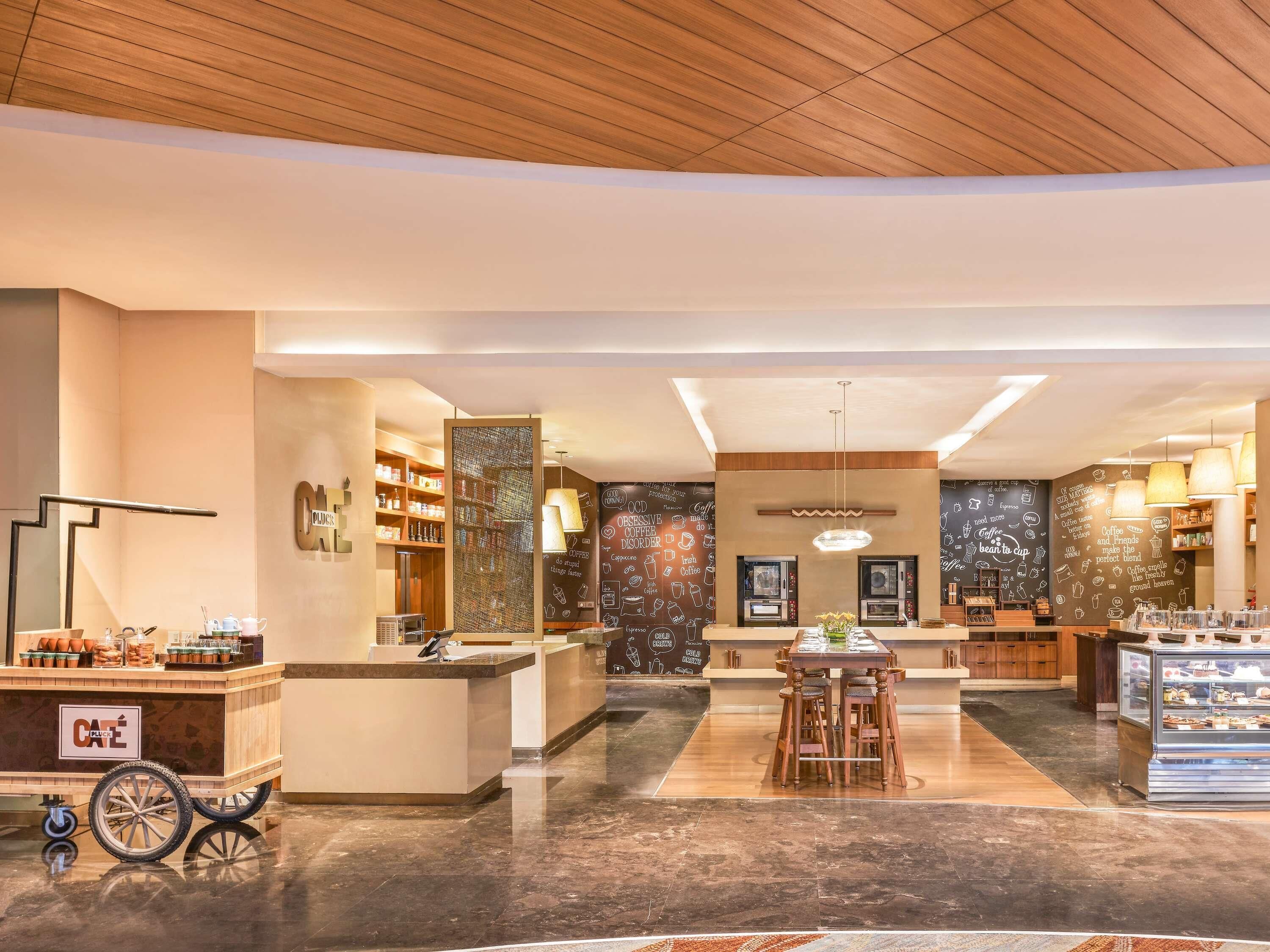 Un interior de cafetería moderno con mostrador central, zona de estar y decoración en la pared.