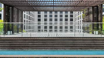 A pool area with a wooden pergola, a tiled deck, and a view of a modern building with a grid-like facade.