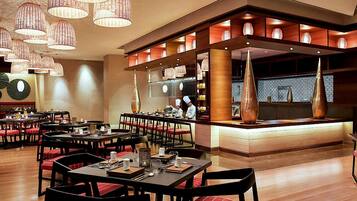 Un restaurante con varias mesas, sillas tapizadas en rojo e iluminación colgante.