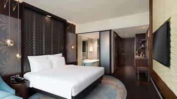 Ein modernes Hotelzimmer mit einem großen Bett, einem Fernseher, einem Schreibtisch und einem Badezimmer.
