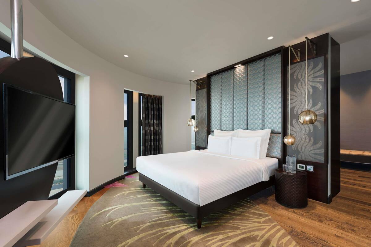 Ein modernes Hotelzimmer mit einem großen Bett, einem Flachbildfernseher, einer dekorativen Wandverkleidung und einem kleinen Beistelltisch.