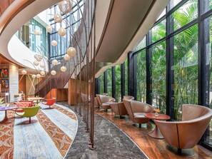 A modern interior with a curved staircase, seating area, and large windows with a view of greenery. - Pullman New Delhi Aerocity Hotel (New Delhi)