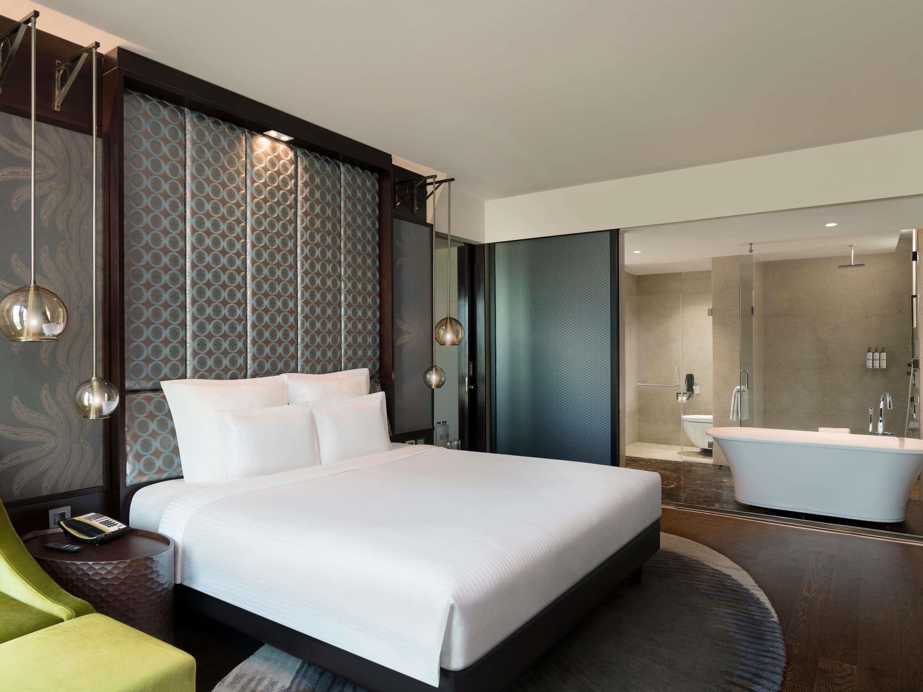 Une chambre d’hôtel moderne dotée d’un grand lit, d’un coin salon avec un fauteuil, d’une salle de bain avec baignoire et douche.