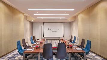 A conference room with a long table, chairs, a projector screen, and a logo on the wall.