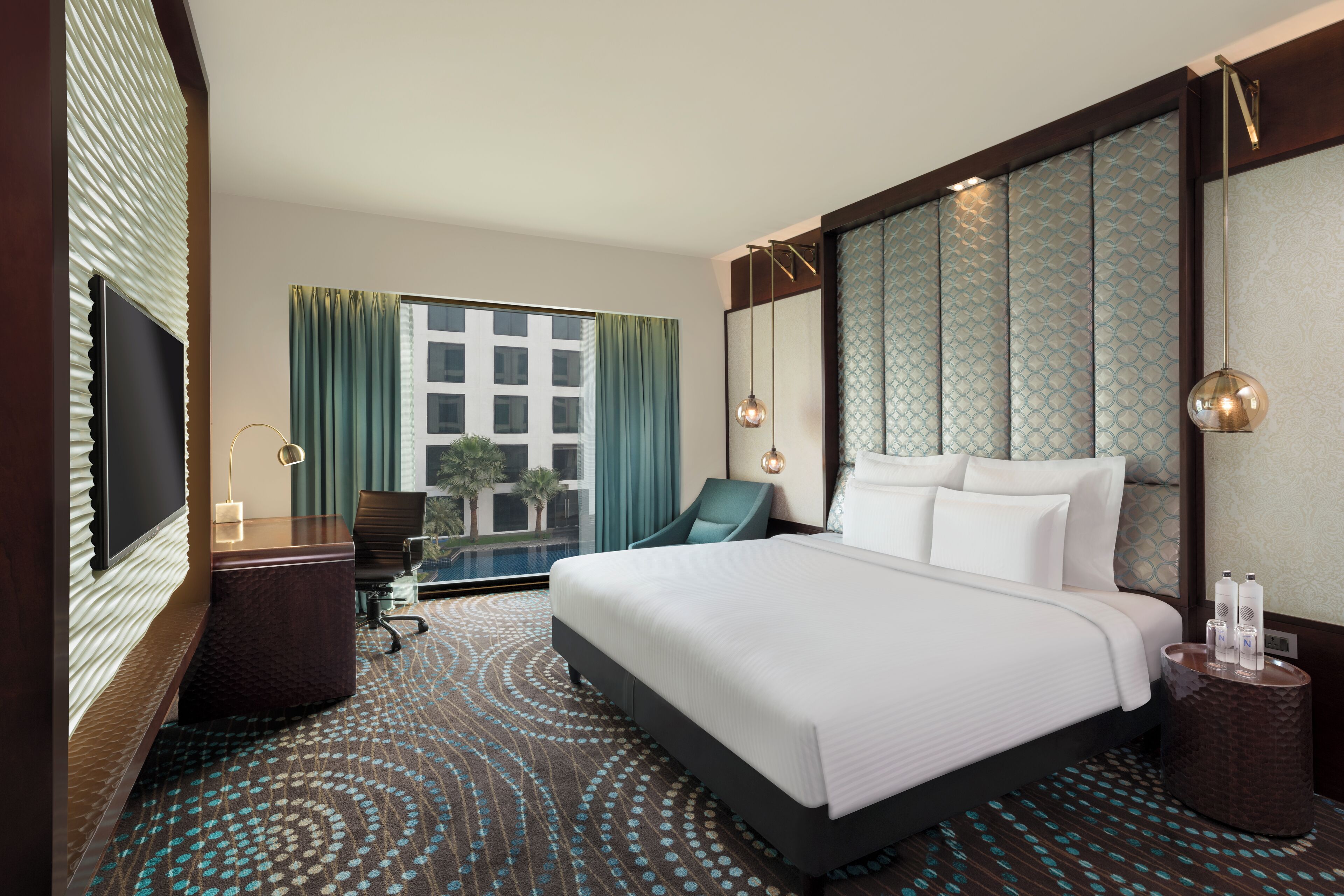 Une chambre d’hôtel avec un grand lit, un bureau, une chaise, une petite table et une vue sur un immeuble par une fenêtre avec des rideaux.