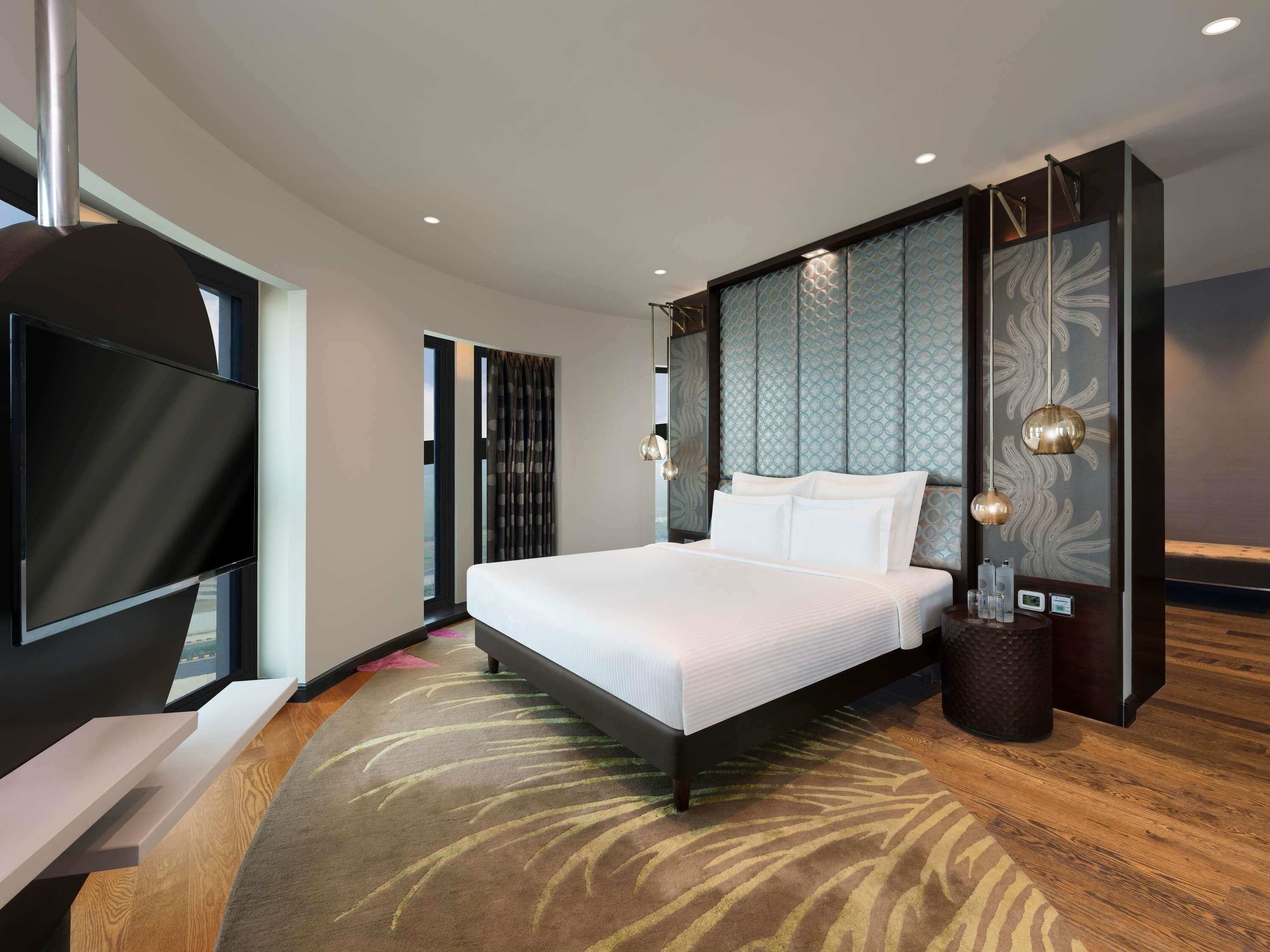 Une chambre d’hôtel moderne dotée d’un grand lit, d’un téléviseur à écran plat, d’un panneau décoratif mural et d’une petite table d’appoint.