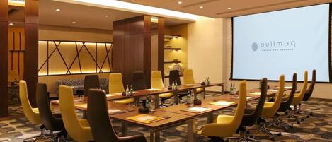 Een vergaderruimte met een lange tafel, gele stoelen en een projectiescherm waarop 'Pullman Hotels and Resorts' staat.