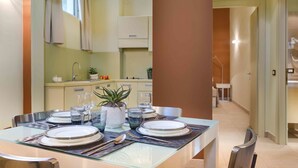A modern dining area with a glass table set for four, surrounded by chairs. A potted plant and a small table with a vase are on the table. - PopArtment (Florence)