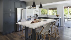 A modern kitchen with grey cabinets, a stainless steel refrigerator, a white island with chairs, and pendant lighting. - Indian Springs Resort & Spa (Calistoga)