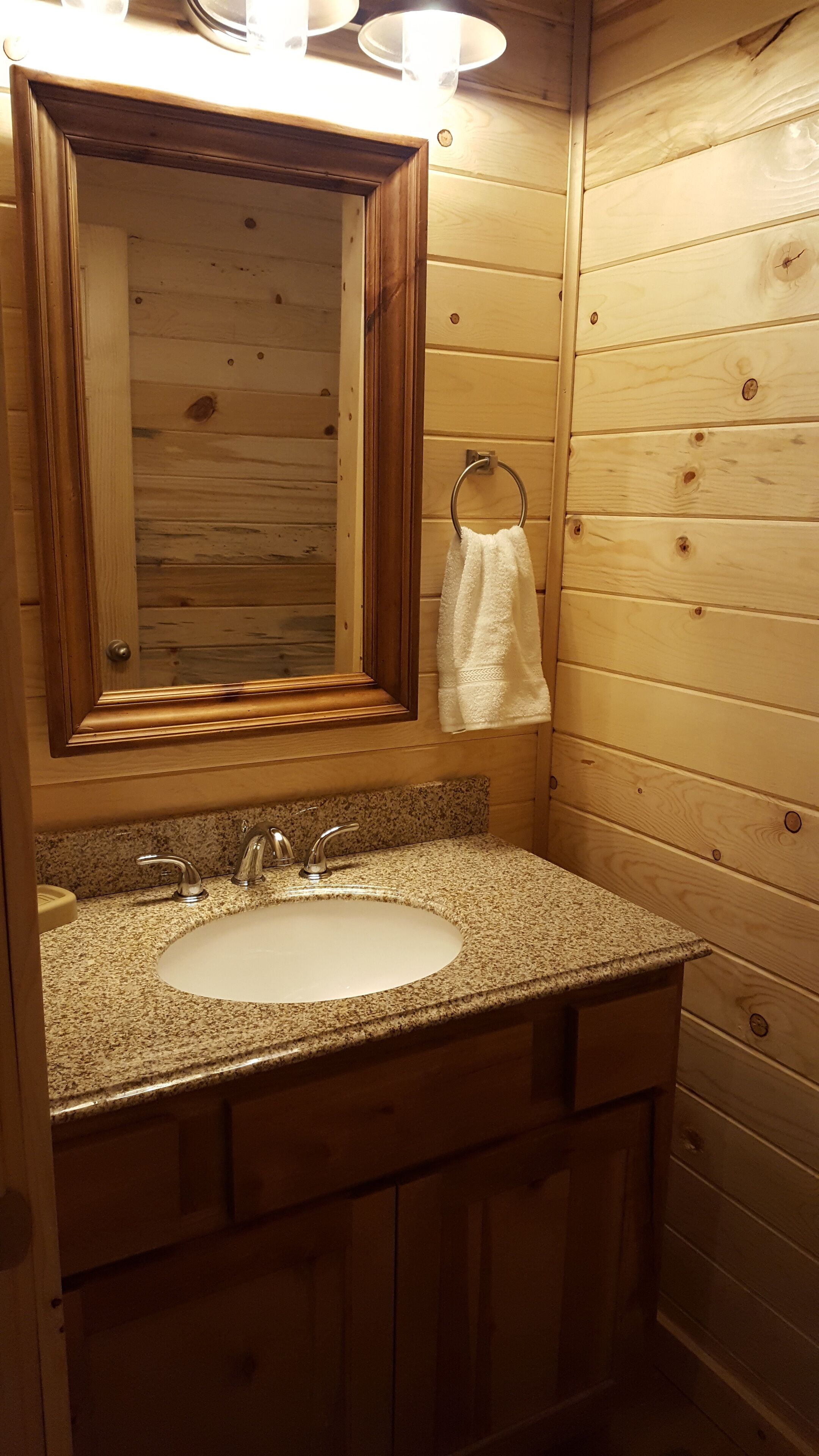 Une salle de bain rustique, avec une cabane en bois, un lavabo en granit, un miroir et une serviette suspendue à un porte-serviettes en métal.