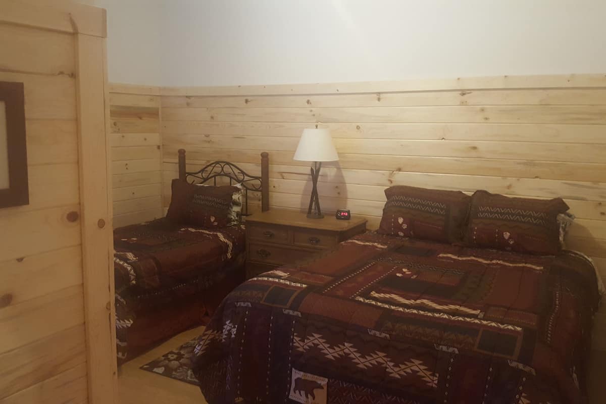 Ein gemütliches Zimmer mit zwei hölzernen Betten, einem Nachttisch mit Lampe und einem gerahmten Bild an der Wand.