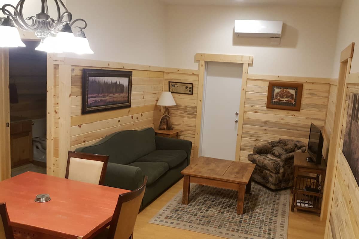 Ein gemütliches Zimmer mit Holzvertäfelung, einem grünen Sofa, einem Holztisch und einem Fernseher.