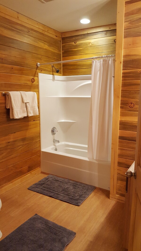 Un baño revestido de paneles de madera con una bañera, una cortina de ducha y dos toallas en un perchero.