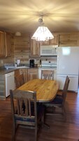 Una cocina con armarios de madera, microondas, estufa, refrigerador y una mesa de comedor con sillas.
