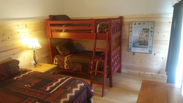 Habitación con literas, suelo de madera, una mesita de noche con lámpara y un cartel en la pared.