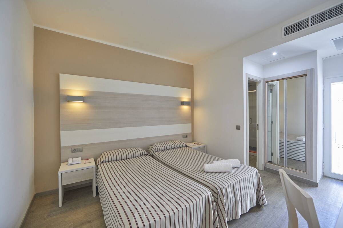 Ein modernes Schlafzimmer mit zwei Betten, einem großen Spiegel und einem begehbaren Kleiderschrank.