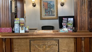 A reception desk with a wooden design, framed artwork on the wall, and a sign indicating street cleaning times. - Hotel Villa Convento (New Orleans)