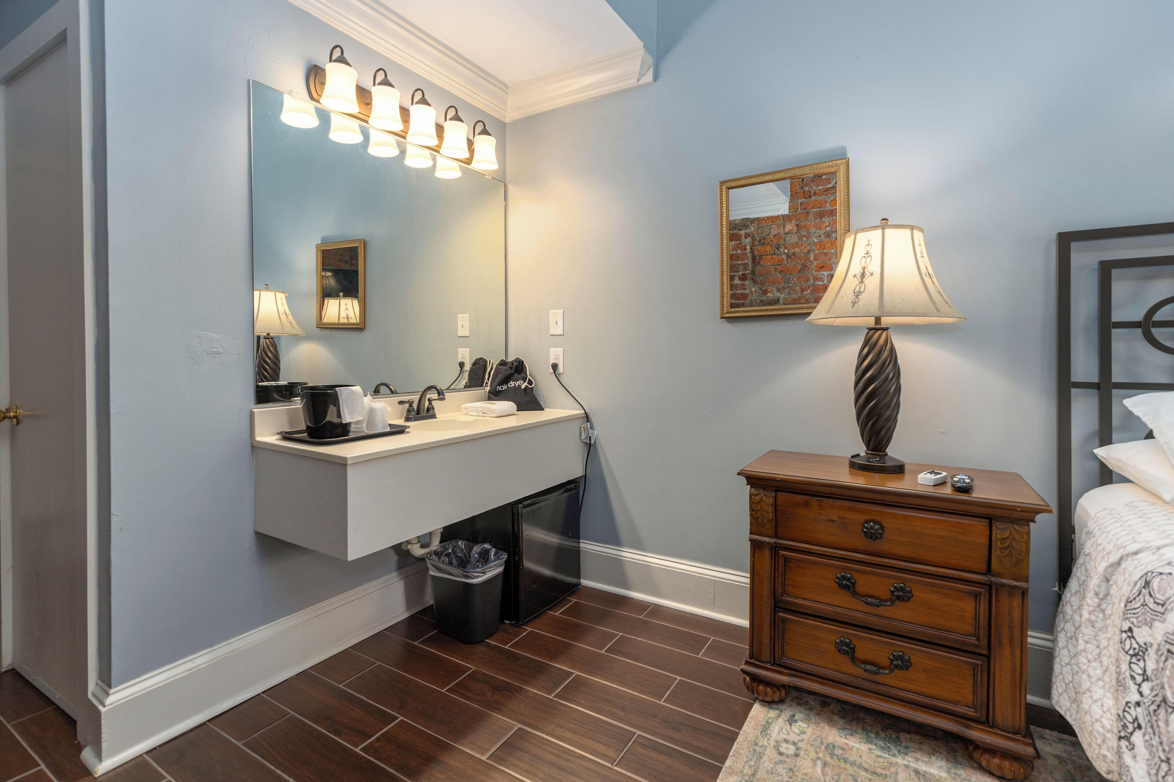 A bathroom with a vanity, mirror, and a bedside table with a lamp.