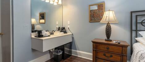 A bathroom with a vanity, mirror, and a bedside table with a lamp.