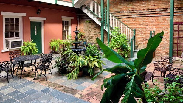 A courtyard with a fountain, outdoor seating, and a brick building with a green door and window numbers. - Hotel Villa Convento (New Orleans)