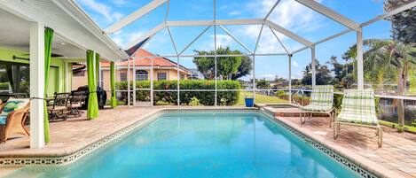 A covered swimming pool with a clear blue water, surrounded by lounge chairs and a patio area.