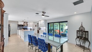 Une cuisine moderne avec des meubles blancs, un four à micro-ondes et un grand îlot central doté de chaises bleues.