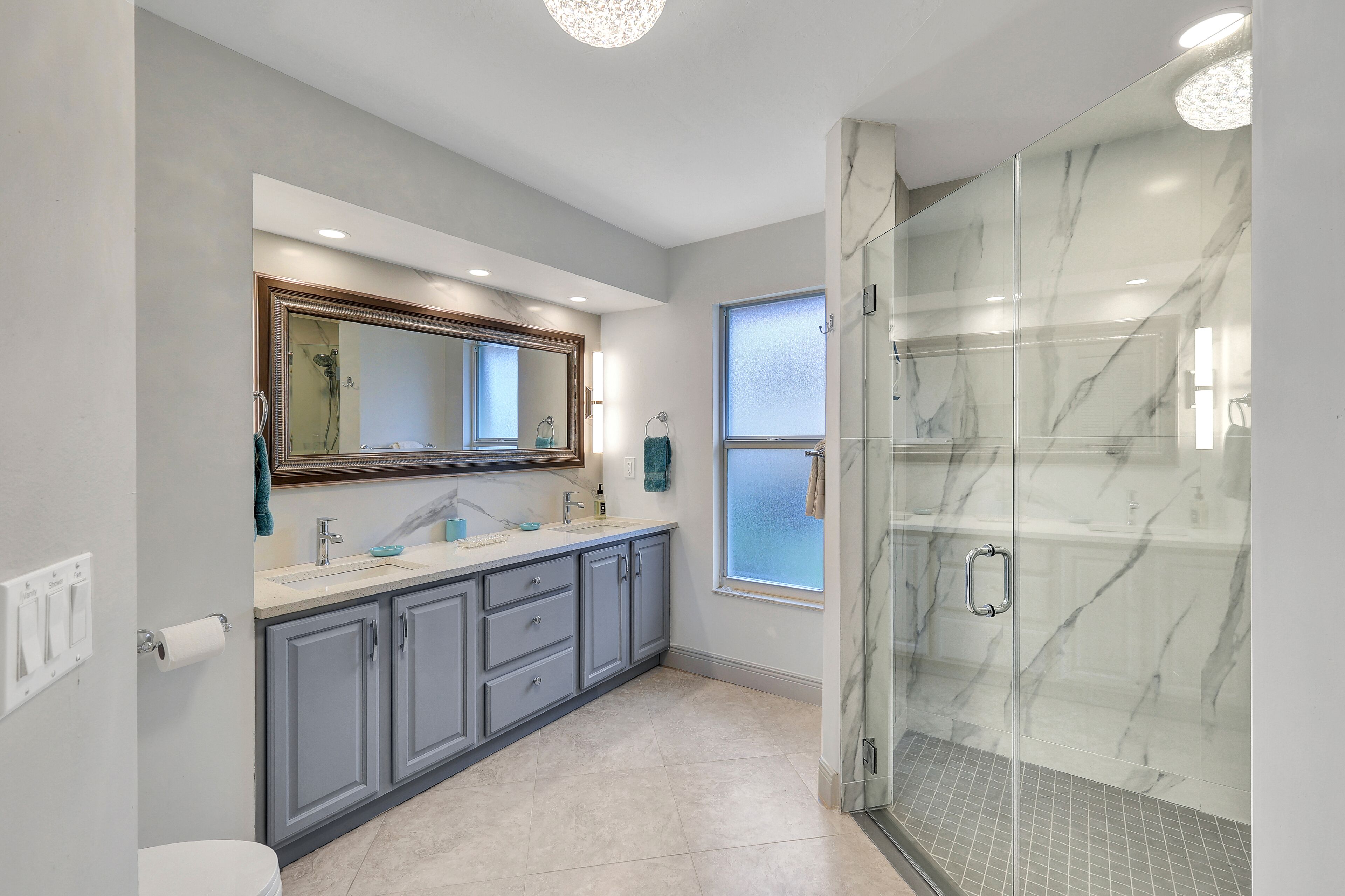 A modern bathroom with a large mirror, dual sinks, and a glass-enclosed shower.