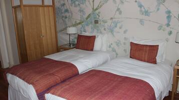 A double bed with white and red bedding, a wooden wardrobe, and a wall with floral wallpaper.